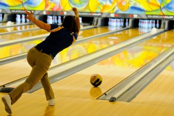 A woman rolling a bowling ball down an alley.