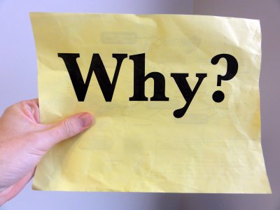 A hand holds a piece of paper with the word 'Why?' printed on it.